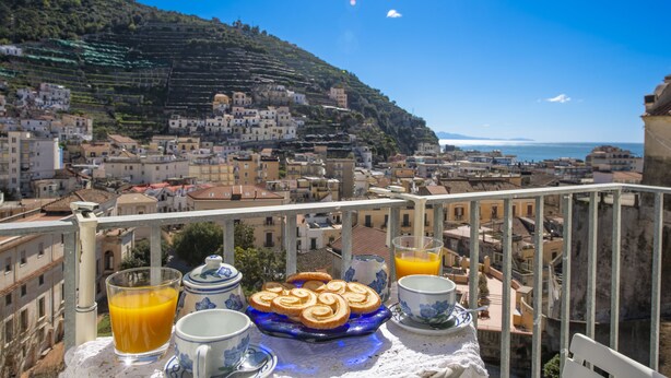 A balcony with a table set for breakfast, overlooking a coastal town with terraced houses and a clear blue sky. - Casa Diodora, vicino al mare, in Costiera Amalfitana (Maiori)