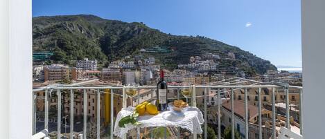 A balcony with a table set for two, overlooking a cityscape with buildings and a hill.