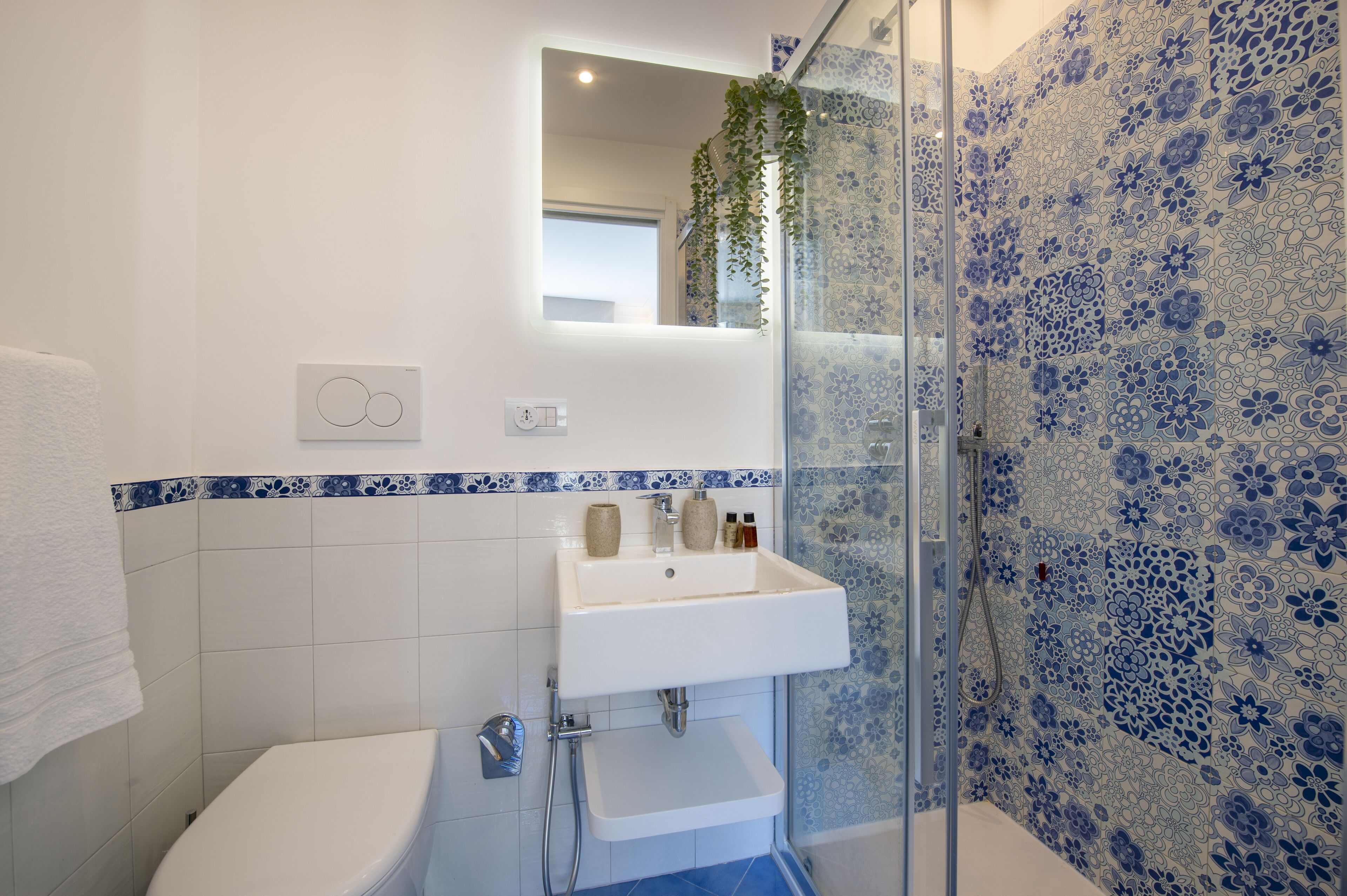 A bathroom with a white sink, a glass shower enclosure, and blue floral tiles.