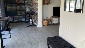 A modern living room with a stone wall, a black sofa, a glass coffee table, and a television.