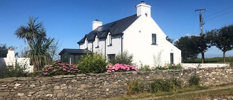 A white house with a stone wall and pink flowers in front.