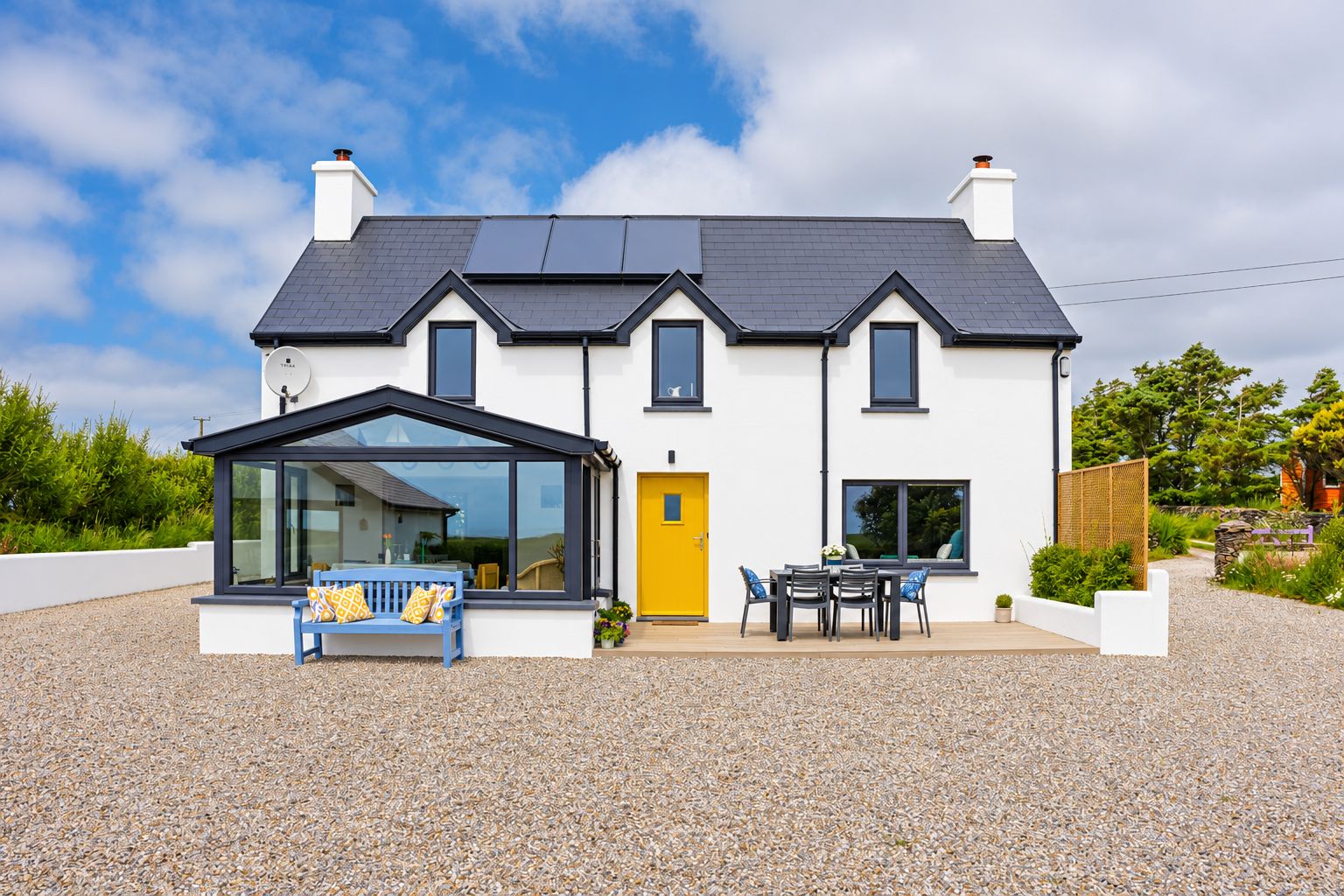 A modern two-story house with a large front porch, a conservatory, and a gravel driveway.