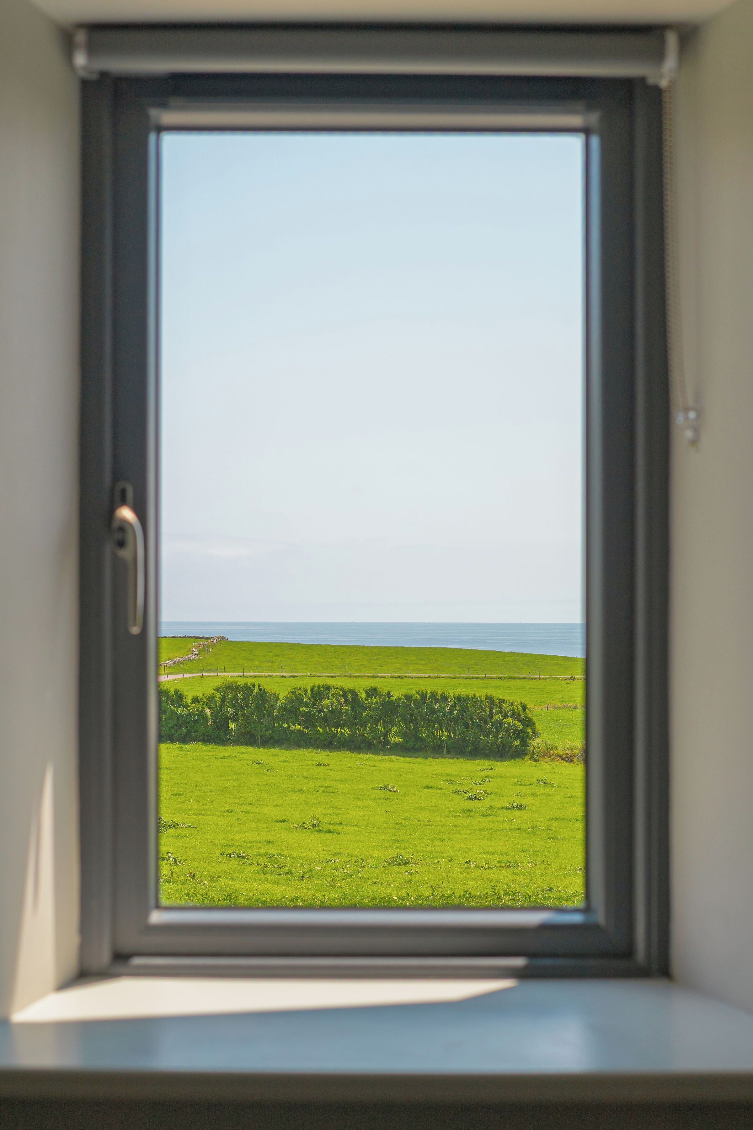 A window with a view of a green field and a body of water.