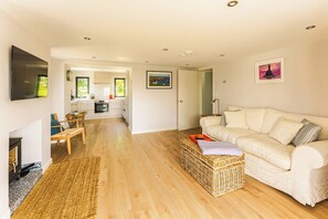 A spacious living area with a sofa, a television, and a kitchen in the background. - 5-star rural escape hidden between the coastal towns of Kinsale and Clonakilty, (Clonakilty)