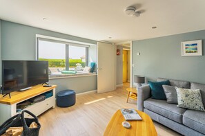 A modern living room with a television, seating area, and a view of a garden through a large window. - 5-star rural escape hidden between the coastal towns of Kinsale and Clonakilty, (Clonakilty)
