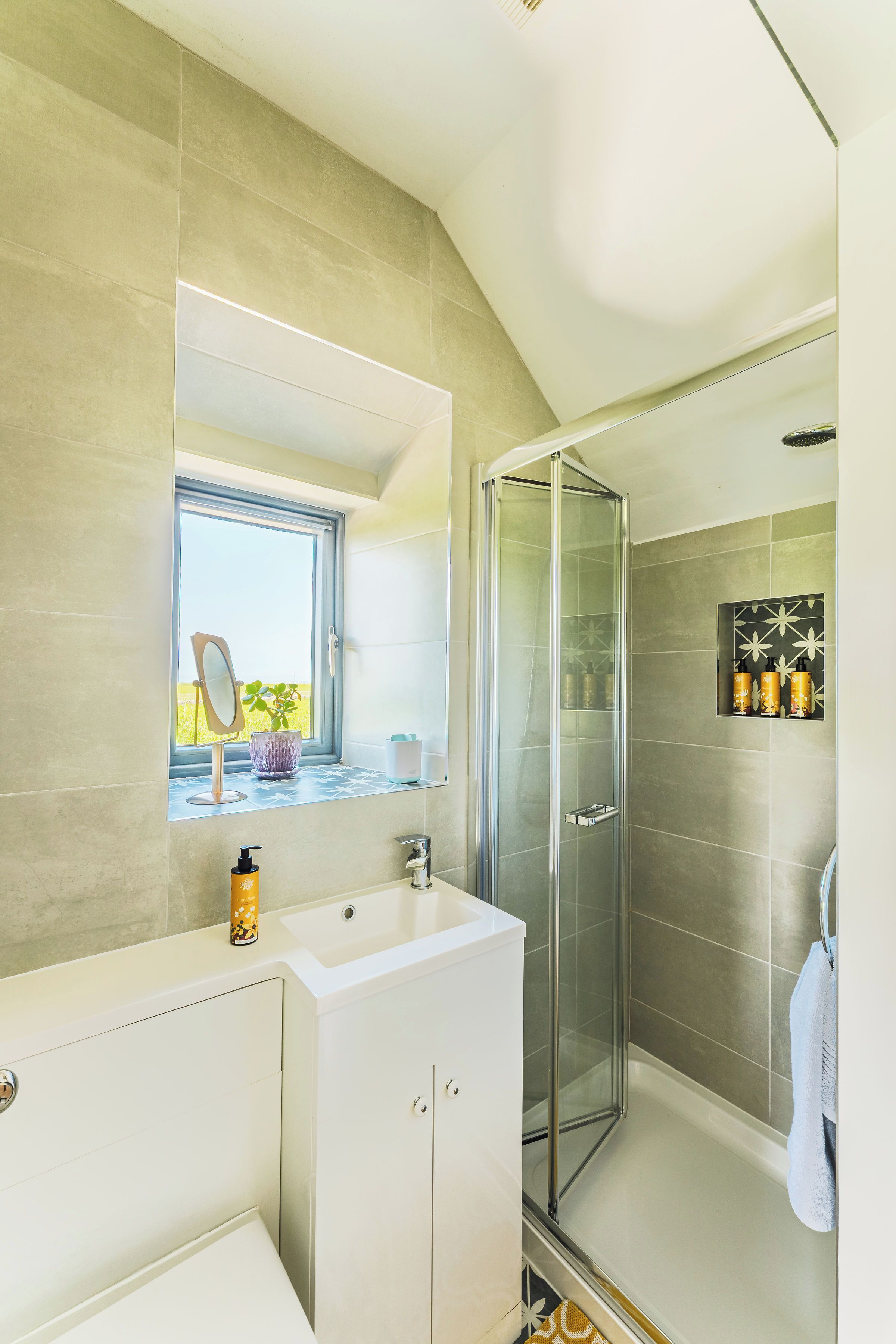 A modern bathroom with a glass-enclosed shower, a large mirror, and a window.