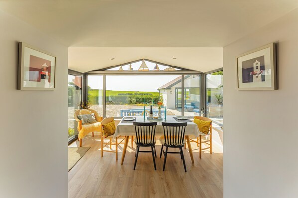 A dining area with a table and chairs, a view of the outdoors, and framed pictures on the walls.