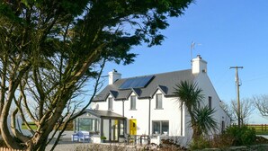 A white house with solar panels, a stone wall, and a bench.