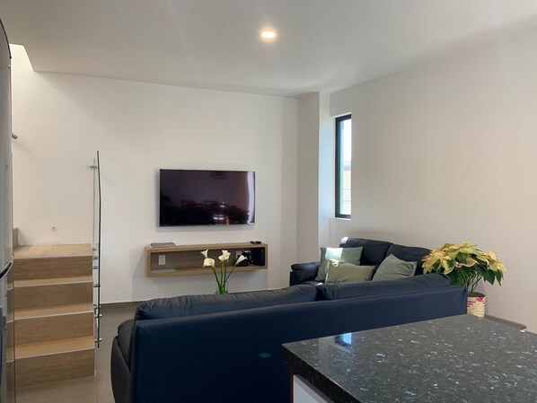 A modern living room with a flat-screen TV, dark blue sofa, and a small coffee table. - Modern 2 bedroom apartment, a short walk from downtown. (Oaxaca de Juárez)