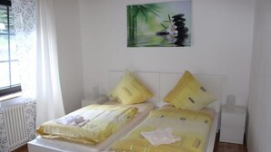 A double bed with yellow bedding, a white headboard, and a painting of a bamboo forest on the wall.