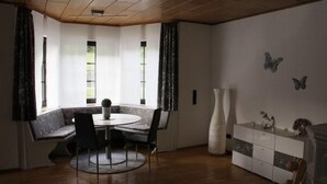 A room with a round table, chairs, a bench, a cabinet, and a window with curtains.