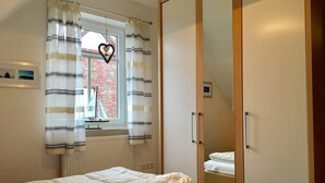 A bedroom with a bed, a window with striped curtains, a heart-shaped decoration, and a mirror on the wall. - Holiday beach chair - centrally located in Norddeich (Norden)