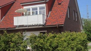 A two-story house with a red-tiled roof, a balcony with a white railing, and a satellite dish on the side. - Holiday beach chair - centrally located in Norddeich (Norden)