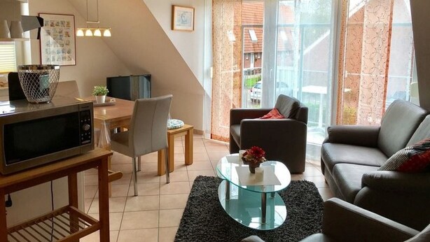A modern living room with a dining area, a sofa, a glass coffee table, and a TV on a wooden stand. - Holiday beach chair - centrally located in Norddeich (Norden)