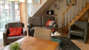 A living room with a sofa, armchairs, a coffee table, and a staircase. - Holiday beach chair - centrally located in Norddeich (Norden)