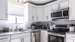 Une cuisine moderne avec des meubles blancs, des appareils en acier inoxydable, un lave-vaisselle, un four à micro-ondes, un grille-pain et une cuisinière.