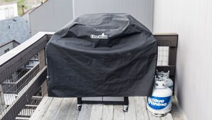 Un barbecue recouvert d’un tissu noir, une bouteille de propane et une rambarde en métal.