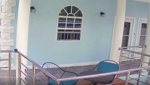 A covered outdoor seating area with a table and chairs, a metal railing, and a window with bars. - La Bwizan Inn Apt. #1 (Laborie)