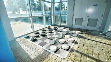 Um tabuleiro de xadrez montado sobre um tapete quadriculado dentro de um quarto com janelas amplas e uma porta.