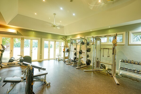 Un gimnasio amplio con diverso equipo de levantamiento de pesas, ventanas grandes y un techo alto.