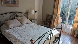 Una cama bien hecha con una colcha estampada, una mesita de noche con lámpara, una silla y una puerta que da a un balcón.