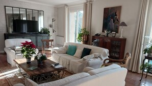 Un salón con sofá blanco, una mesa de centro de madera y un televisor sobre una pared de ladrillo.