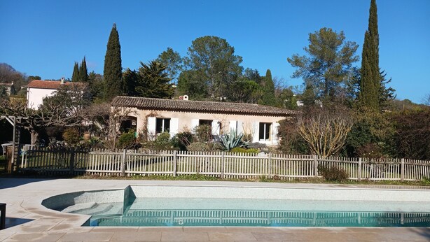 Una casa con piscina, rodeada por una valla de madera y árboles altos.