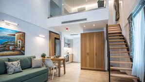 A modern living room with a green sofa, wooden dining table, and a staircase leading to an upper level.