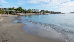 A beach with a calm sea, a sandy shore, and buildings in the background.