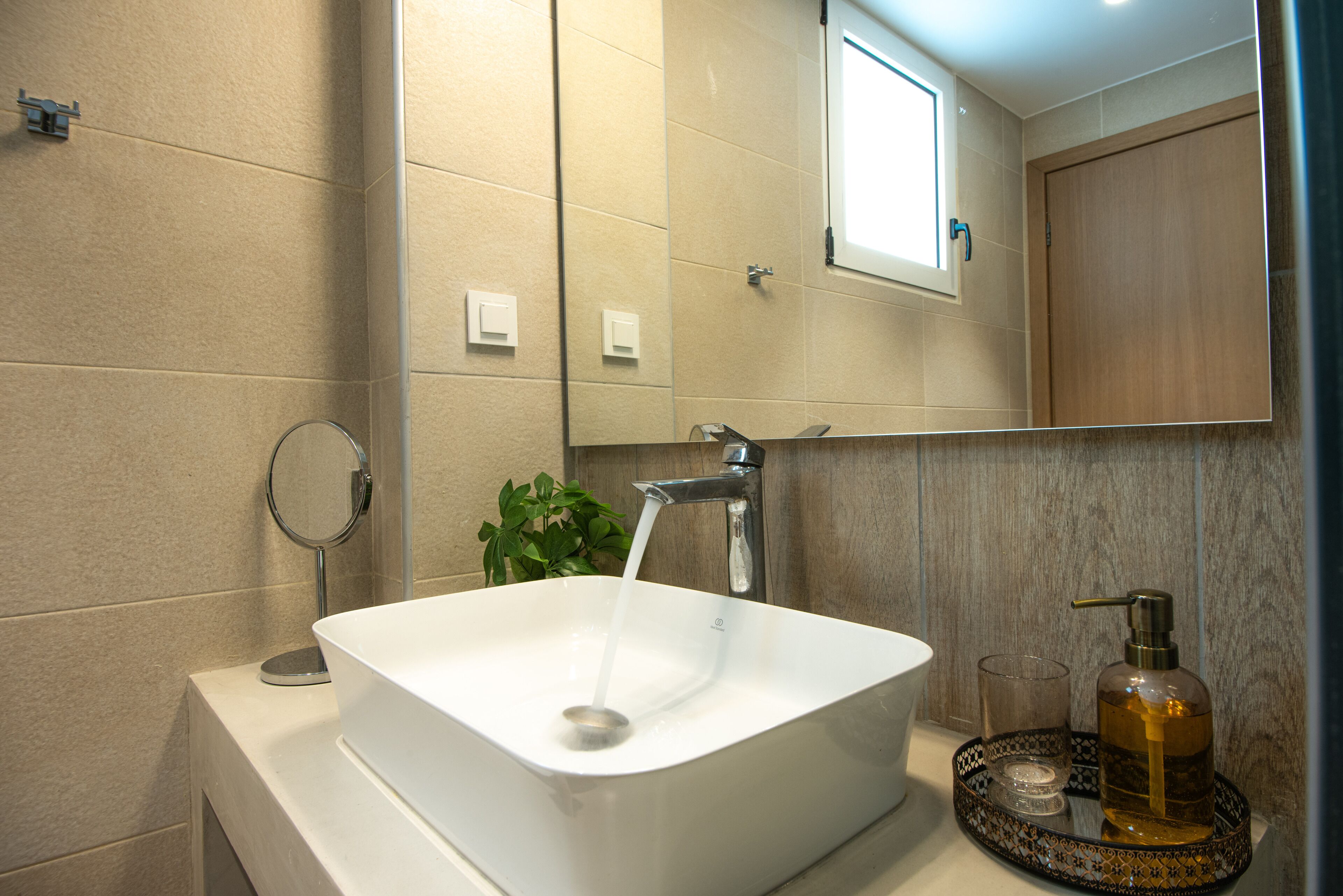 Une salle de bain avec un lavabo blanc, un miroir et une fenêtre située au-dessus du miroir.