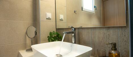 Une salle de bain avec un lavabo blanc, un miroir et une fenêtre située au-dessus du miroir.