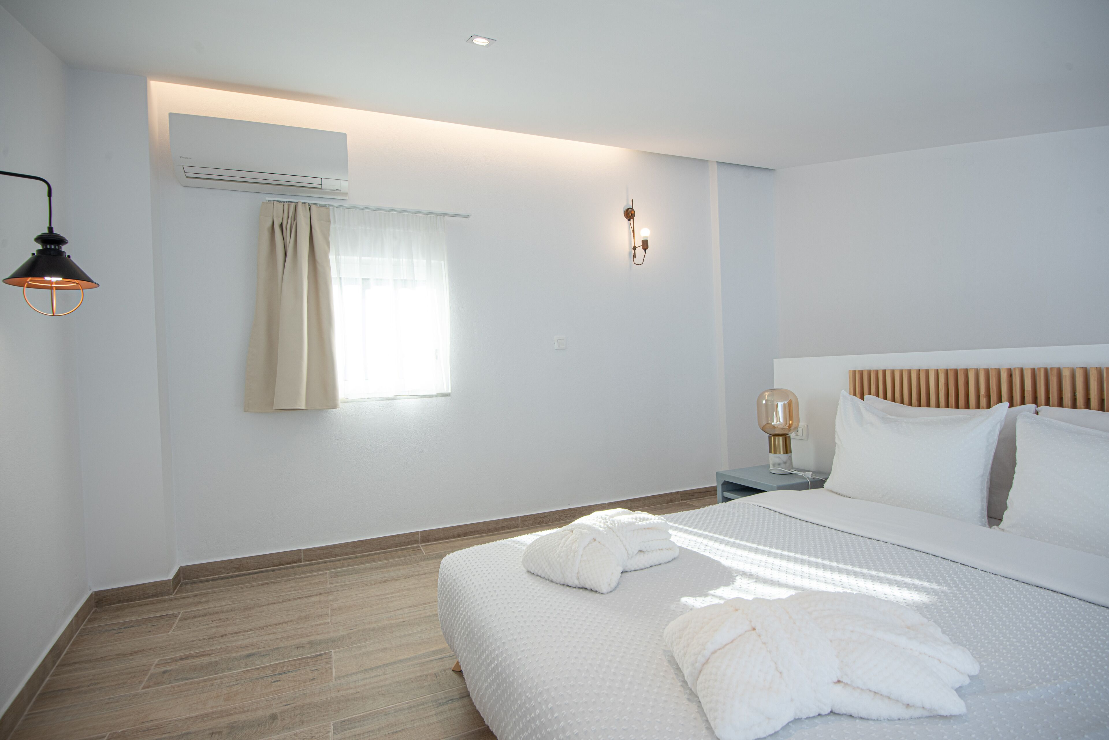 Une chambre d’hôtel moderne dotée d’un grand lit, d’une table de chevet, d’un climatiseur, d’une lampe fixée au mur et d’une fenêtre avec des rideaux.