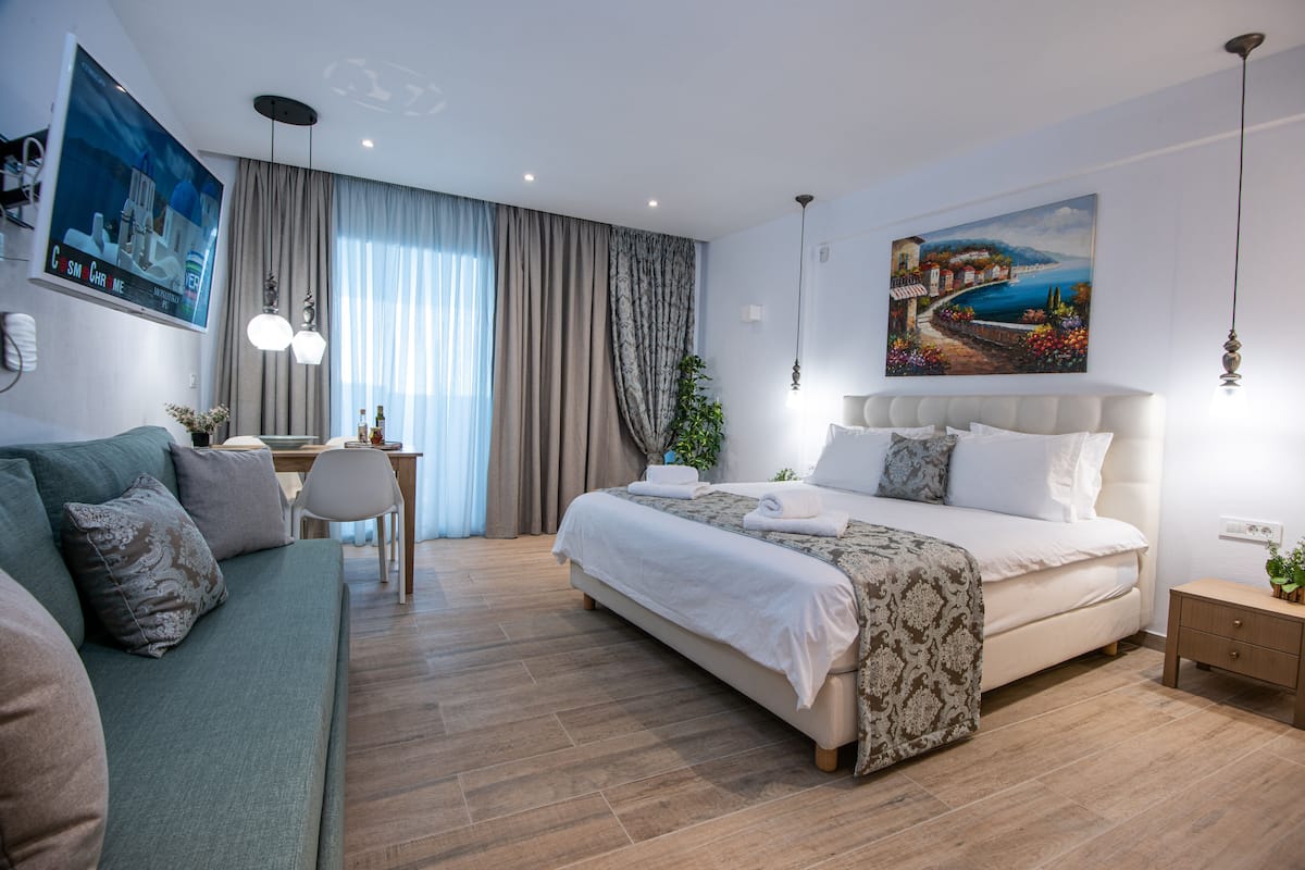 Habitación de hotel moderna con una cama grande, un sofá, un escritorio y un cuadro de una escena costera.