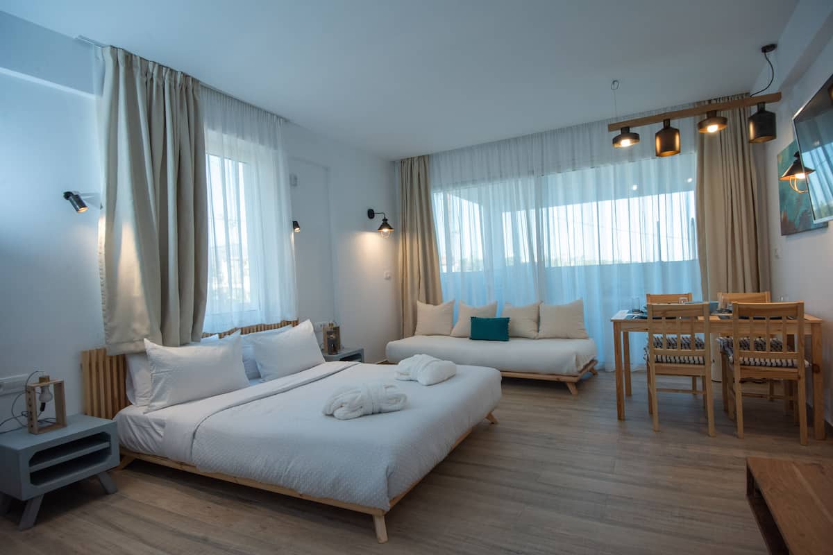 Una habitación de hotel moderna con dos camas, un área de comedor y un ventanal con cortinas.