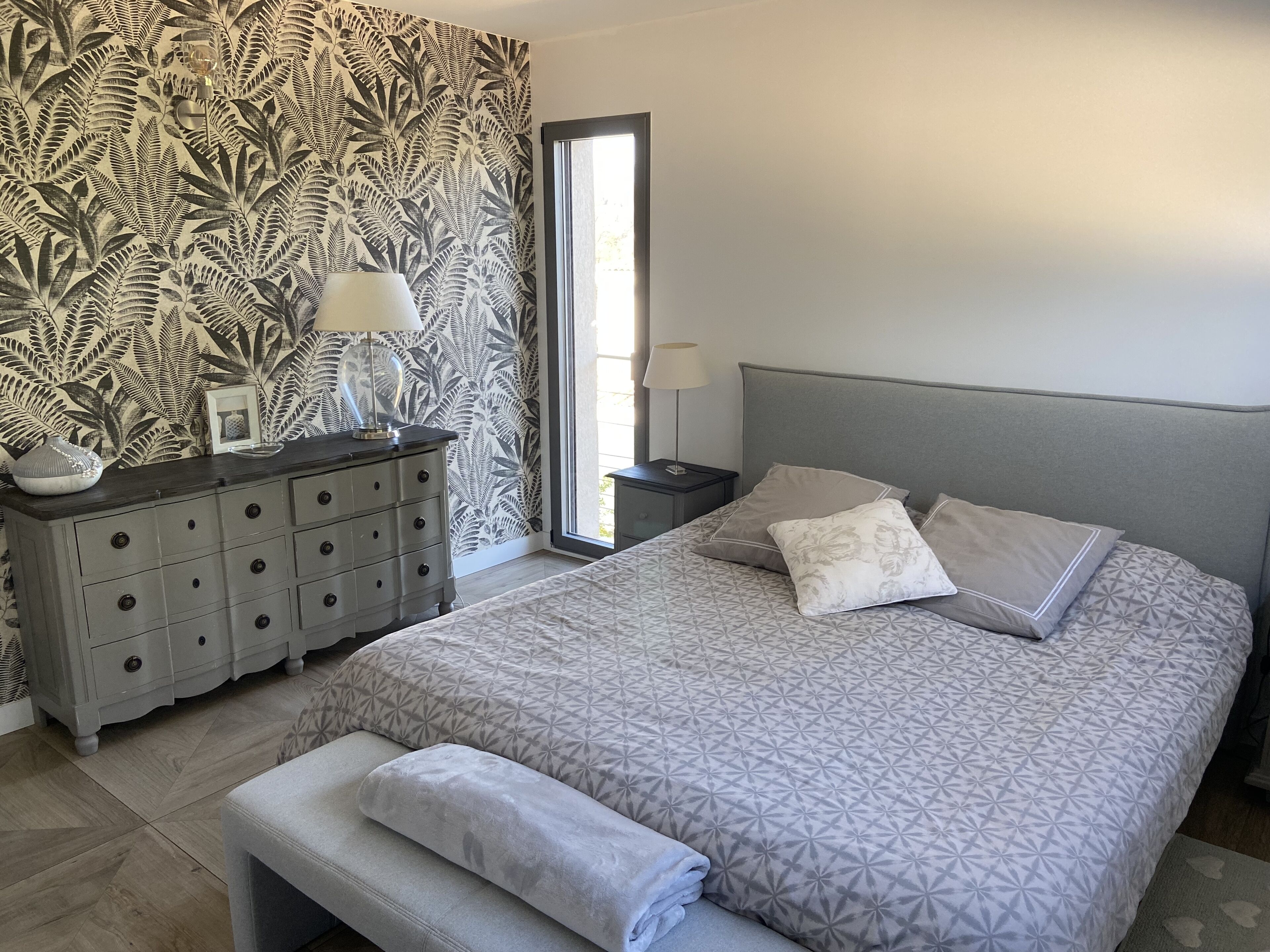 A bedroom with a bed, a nightstand, a dresser, and a window.
