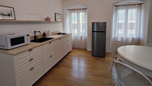 A modern kitchen with a microwave, sink, and refrigerator. There is a dining table with chairs and a chandelier. - 2-bedroom, 4-guest apartment in historic area of Trieste in 19th century style (Trieste)