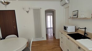 A compact kitchen with a white microwave, a black sink, and a wooden countertop. There is a white chair and a table in the dining area. - 2-bedroom, 4-guest apartment in historic area of Trieste in 19th century style (Trieste)