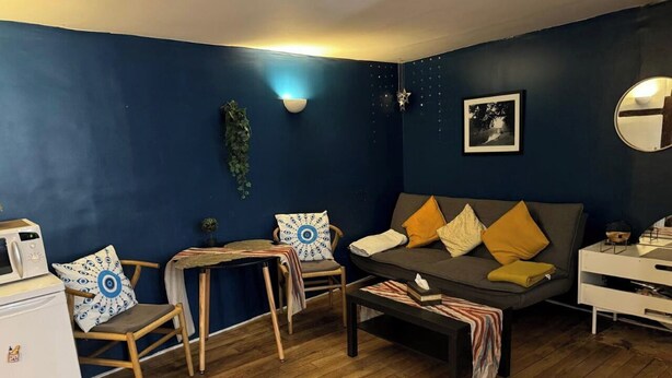 Een gezellige woonkamer met een bank, stoelen, een salontafel en een kleine witte koelkast.