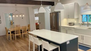A modern kitchen with a central island, white cabinetry, stainless steel appliances, and pendant lighting. - Downtown Wolfeboro! Walk to the lake, restaurants and park (Wolfeboro)