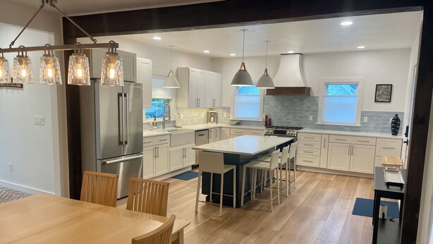 A modern kitchen with white cabinets, stainless steel appliances, and a central island with bar stools. - Downtown Wolfeboro! Walk to the lake, restaurants and park (Wolfeboro)