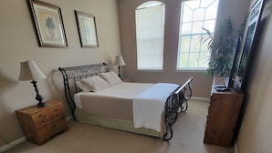 Une chambre à coucher comprenant un lit, deux tables de chevet, une commode et deux fenêtres.