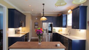 A modern kitchen with dark blue cabinets, stainless steel appliances, and a wooden island with a vase of flowers. - Masters Oasis Tournament Rental (Evans)