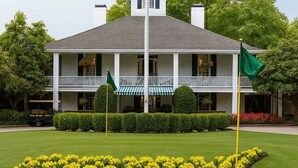 A two-story building with a balcony, surrounded by well-manicured lawns and a distinctive yellow flower bed. - Masters Oasis Tournament Rental (Evans)