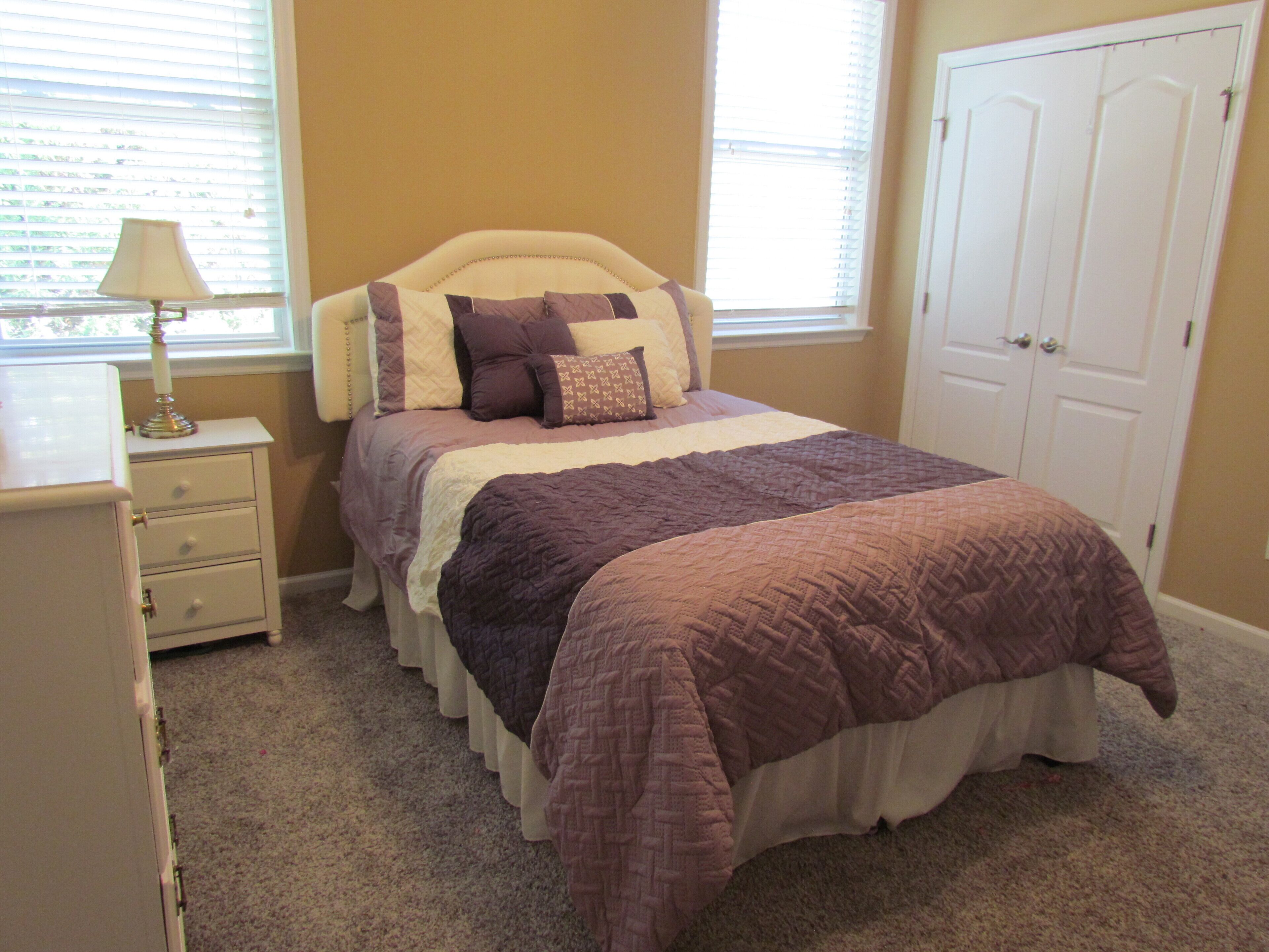 A bedroom with a bed, a nightstand, a lamp, and a door.