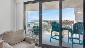 Ein Balkon mit Blick auf den Ozean, einer Couch und türkisfarbenen Stühlen.
