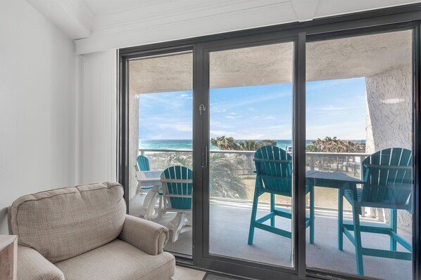 A balcony with a view of the ocean, a sofa, and teal chairs.