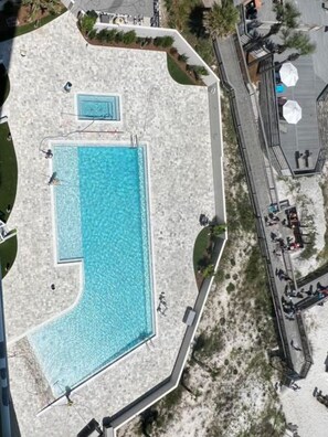 Vue aérienne d’un espace piscine comprenant une piscine rectangulaire, une piscine plus petite et une terrasse avec des parasols.