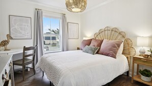 Un dormitorio con una cama grande, un escritorio, una silla, un cabecero de mimbre y vistas al exterior.