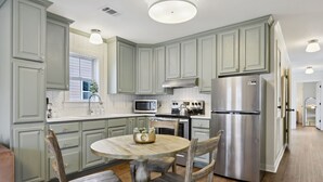 Una cocina con armarios verde claro, un refrigerador de acero inoxidable, un microondas y una mesa de comedor de madera con sillas.