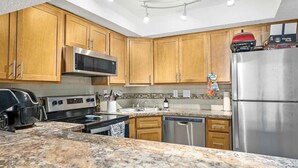 A modern kitchen with wooden cabinets, stainless steel appliances, granite countertops, and a built-in microwave. - Pelican Inlet - Cozy Beach Condo!1 block from the beach! Sleeps 6. Pool/Tennis (St. Augustine)